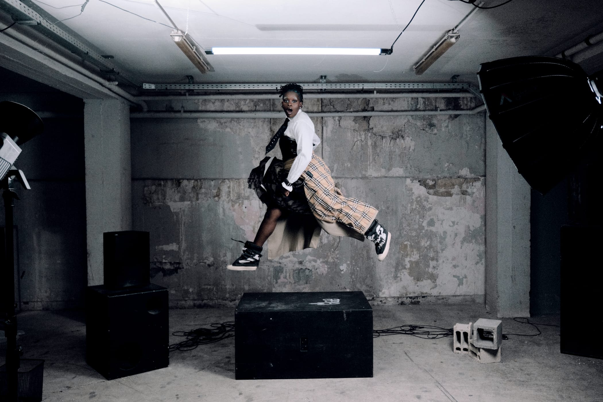 Ezek mid-jump over the black block, trench and skirt flying, sneakers off the floor